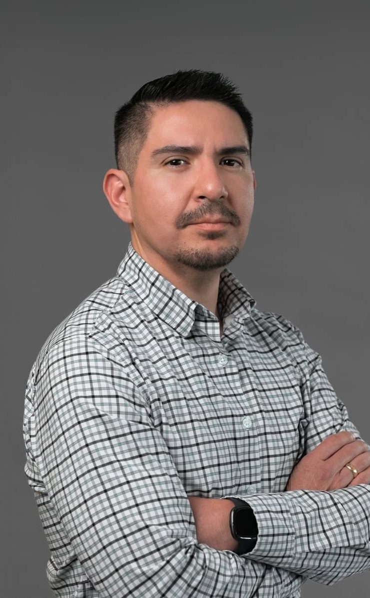 Hector Herrera, arms crossed, in a checked shirt against a gray studio background